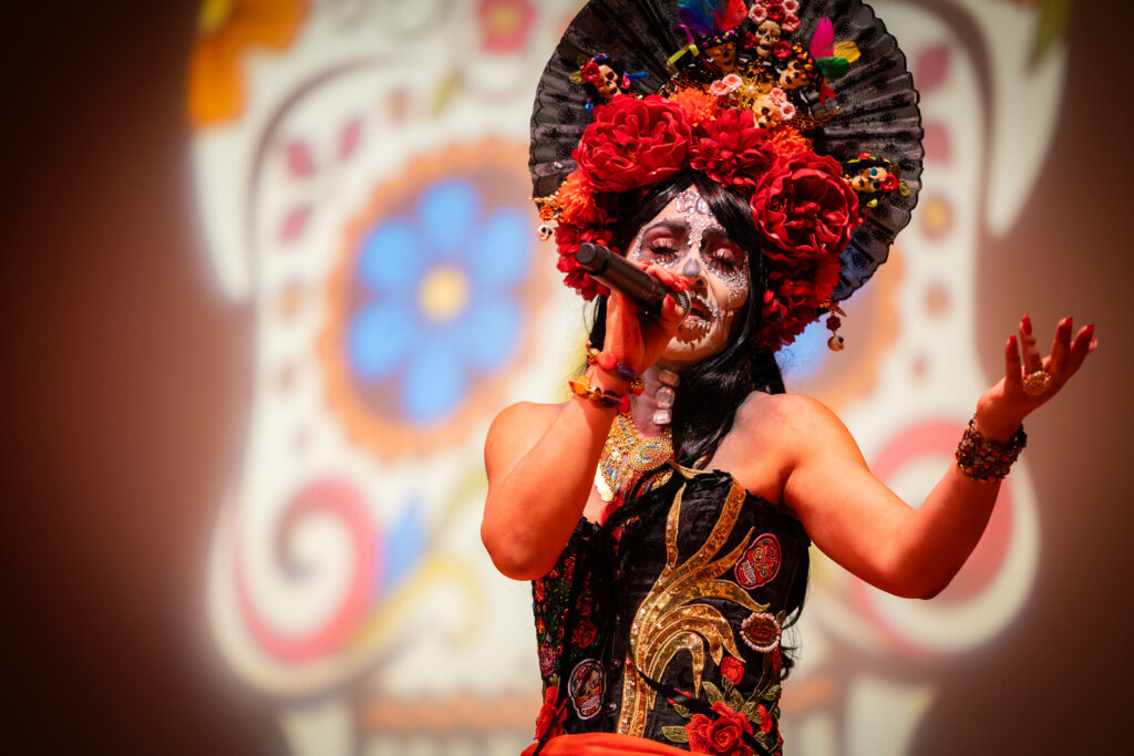 A singer in Dia de la Muertos and sugar skull makeup sings into a microphone
