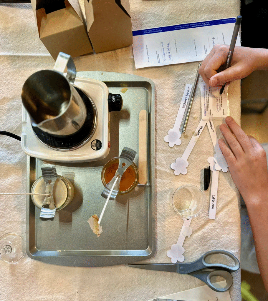 Top of a candle making work bench with supplies and a pair of hands writing labels