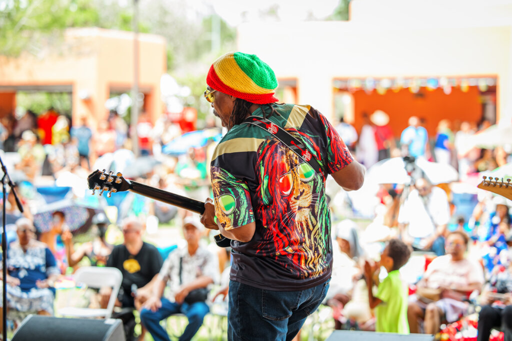 A reggae performer plays a guitar to a crowd.