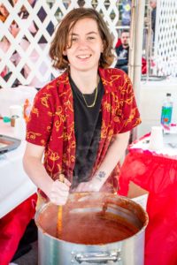 An image of a different person stirring a big pot of sauce 
