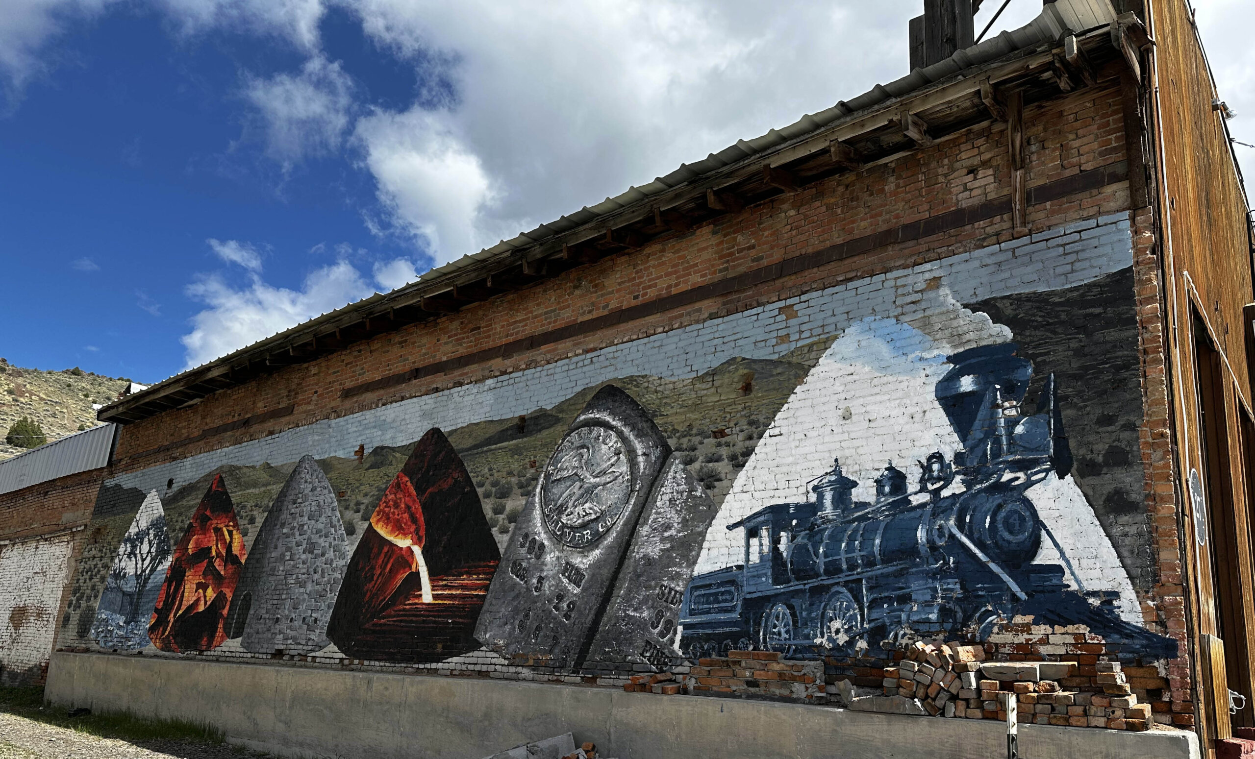 Erik Burke mural in Eureka includes a lone pinion pine, a pinion pine in the charcoal oven, and the oven itself, silver ore and a close up of a bar of Nevada silver, and the E and P Engine No. 4 used to haul ore from Eureka to the station in Palisade.