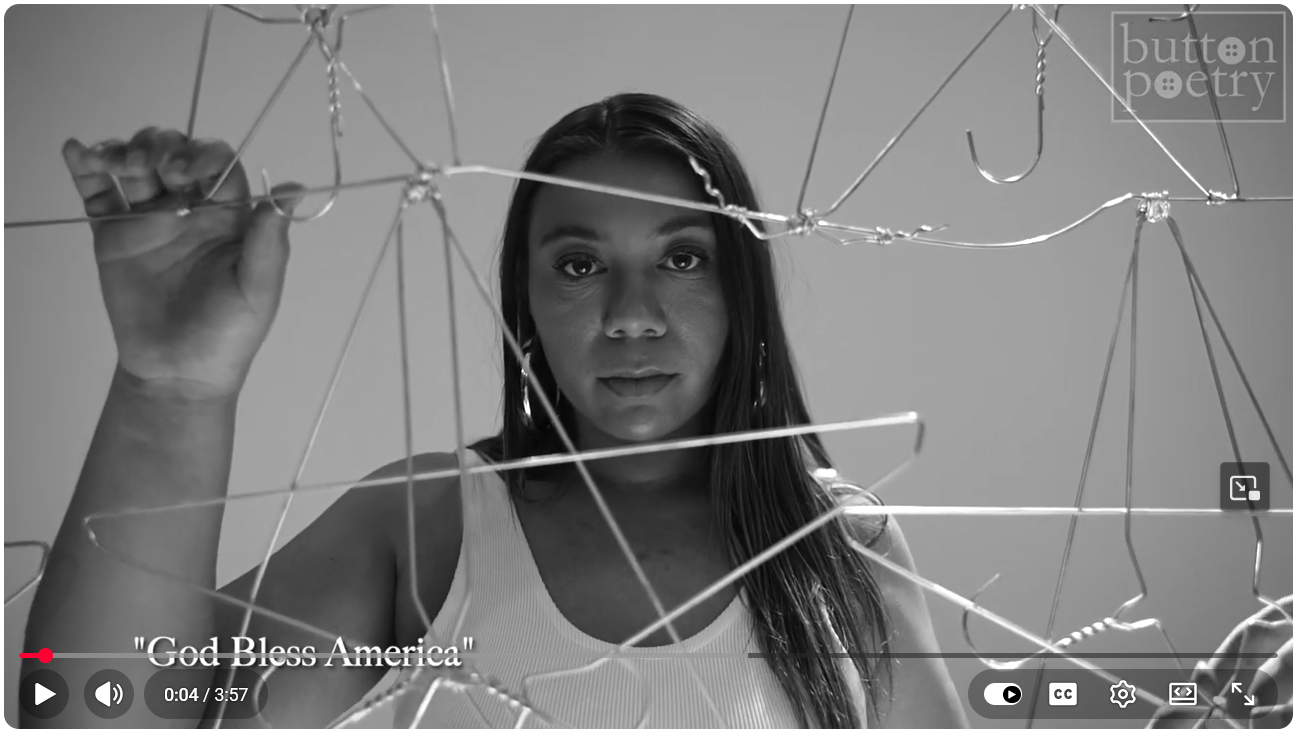 A woman stands behind twisted wire hangers, looking directly at the camera in a black-and-white scene. The text on screen reads God Bless America and button poetry.