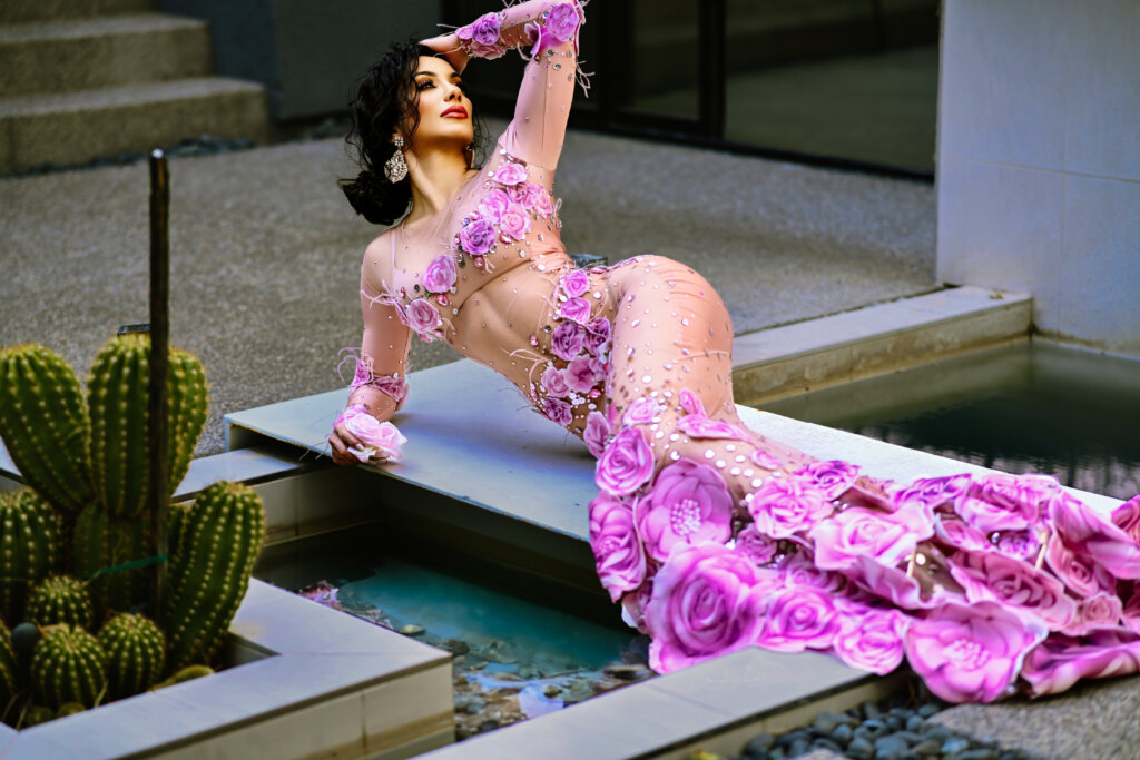 A woman in a long, fuchsia color lacy dress in a seductive pose.