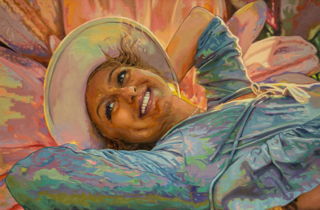 A smiling person wearing a wide-brimmed hat and a blue shirt reclines with hands behind their head, surrounded by warm, colorful, flower-like abstract shapes in the background.