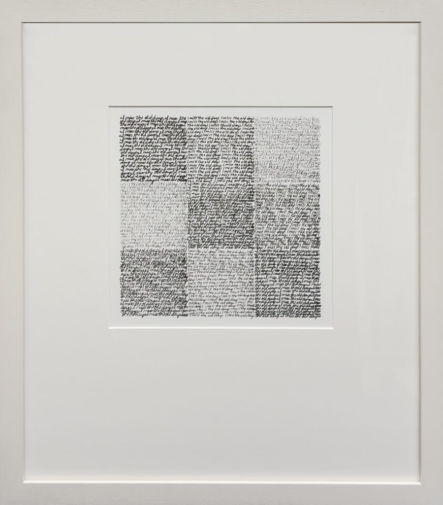 A framed artwork featuring a grid of nine squares filled with dense, handwritten text in black ink. The handwriting forms different shades, creating a checkerboard pattern within a white mat and frame.