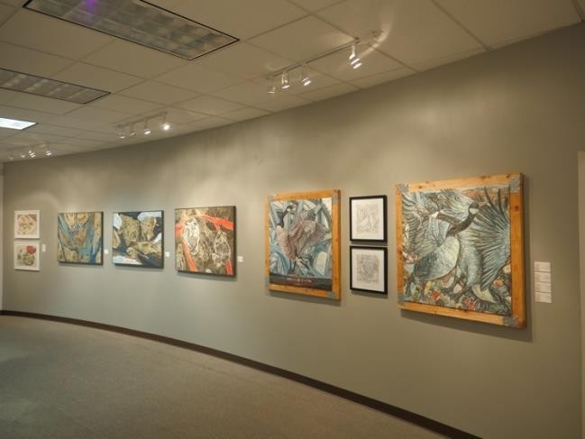 A hallway art exhibit features six framed paintings with intricate abstract designs and a bird motif.
