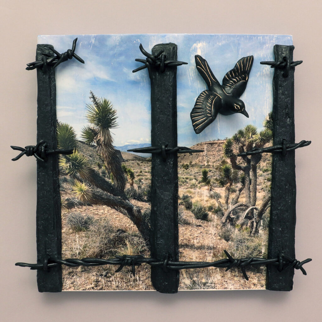 A relief art piece shows a desert scene with Joshua trees behind black sculpted bars and barbed wire, with a raised black bird in flight above, creating a sense of separation from nature.