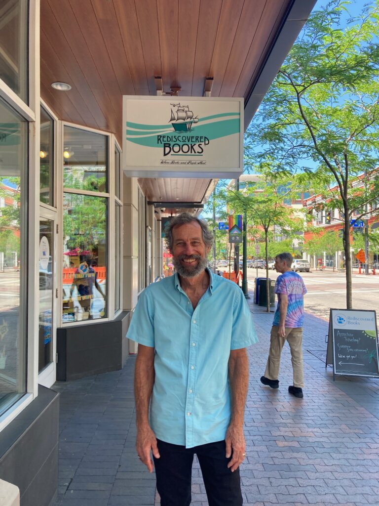 Shaun Griffin standing under a shop sign for Rediscovered Books.
