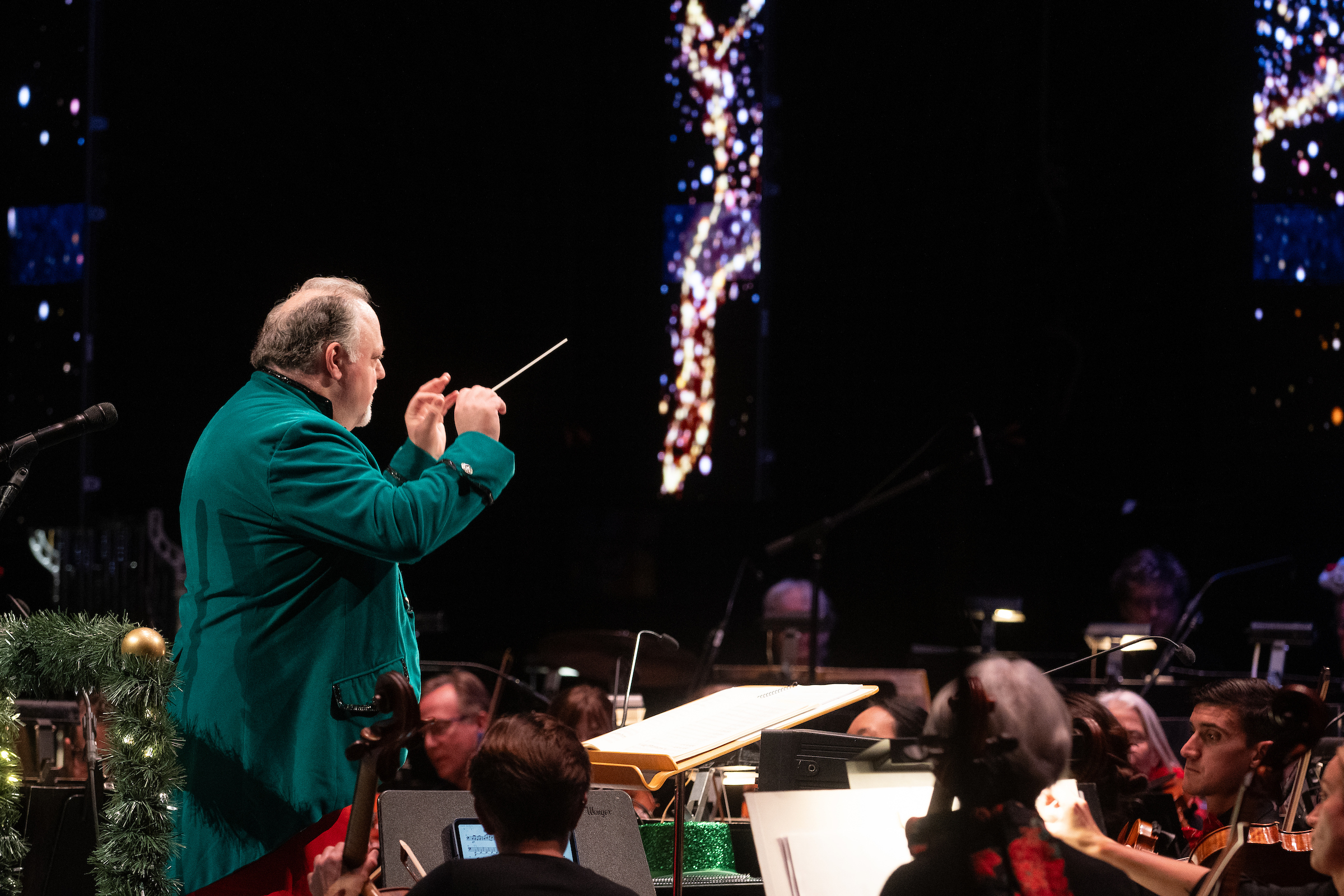 A conductor dress in a green jacket leads an orchestra.