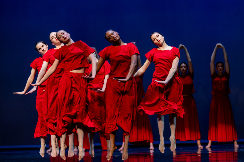 Dancers in red do a hop move in the choreography