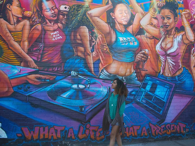 a woman stands in front of a colorful mural showcasing vibrant artwork and intricate designs