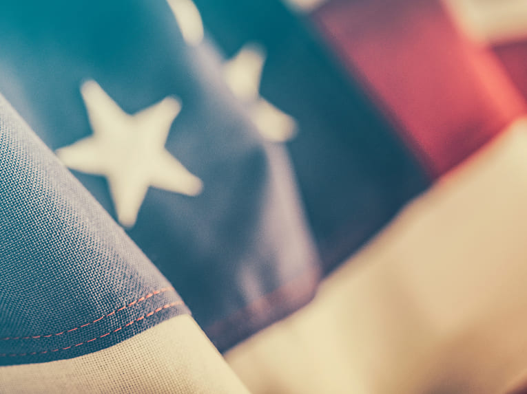 Close-up of a section of the American flag, showing part of the blue field with white stars and a hint of red and white stripes, with soft focus and natural lighting.