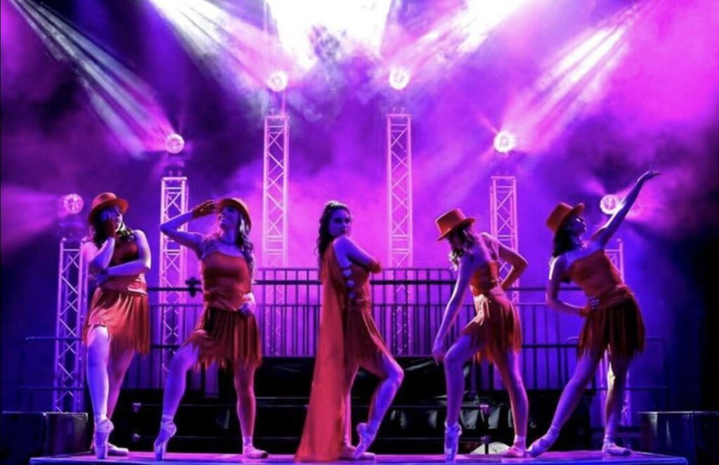 Five performers in red outfits and hats under spotlights