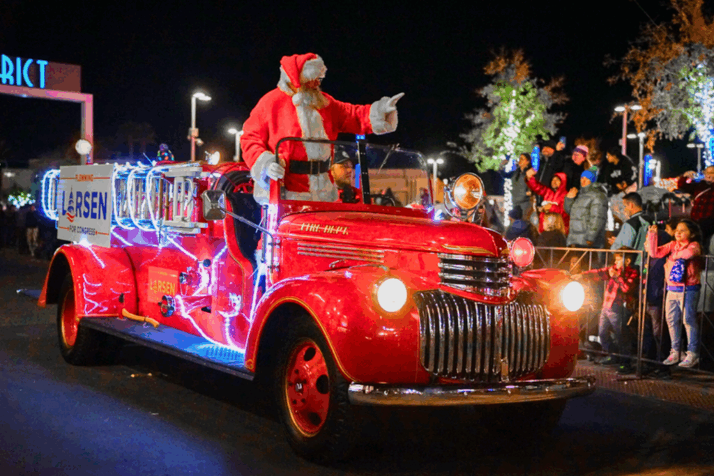 Santa in a old school fire truck waves to a parade crowd at night