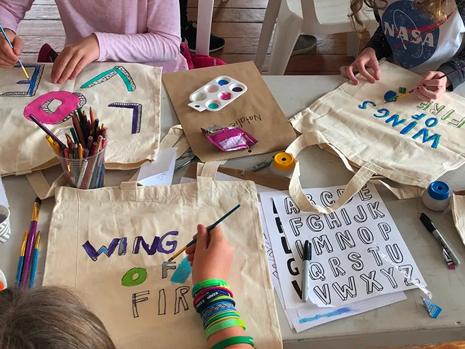 Children painting canvas bags with vibrant colors, using brushes and markers