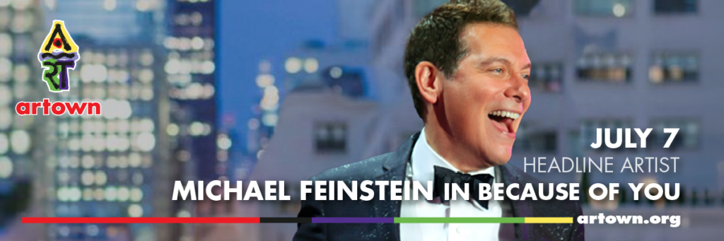 A smiling man in a tuxedo sings on stage with cityscape decor behind him. Text reads: artown, JULY 7 HEADLINE ARTIST, MICHAEL FEINSTEIN IN BECAUSE OF YOU, artown.org with a colorful logo on the left.